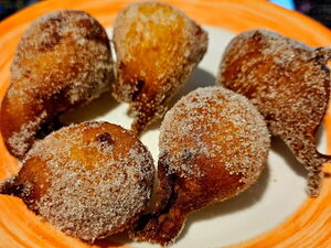 Orangenbälle. Quarkbällchen ähnlich mit Zucker bestreut. Liegen auf einem Teller mit Orangenen Rand.