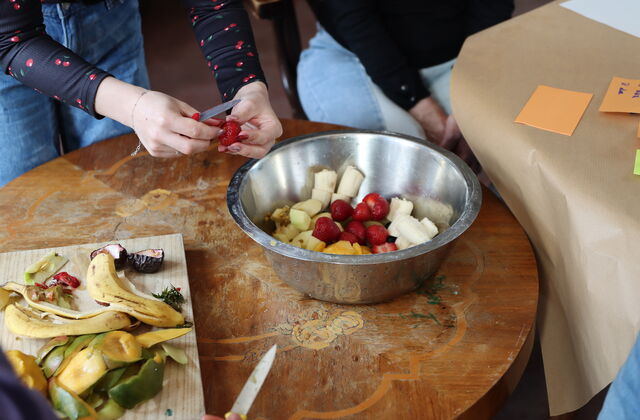 Erdbeeren, Bananen und Ähnliches wird in eine Schüssel geschnippelt.
