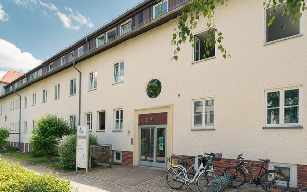Eingangsbereich eines Hauses mit heller Fassade. Rechts neben dem Eingang ein Fahrradständer.