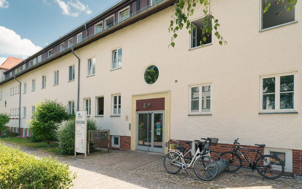 Eingangsbereich eines Hauses mit heller Fassade. Rechts neben dem Eingang ein Fahrradständer.