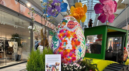 Im Sterncenter. Osterdekoration im Gang. Trecker mit Anhänger. Im Anhänger großes Osterei. Blumen und der Osterhase.