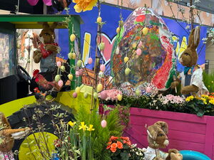 Osterdekoration. Trecker mit Anhänger. Auf dem Anhänger ein großes Osterei. Alles hübsch mit Blumen bepflanzt. Osterhasen.