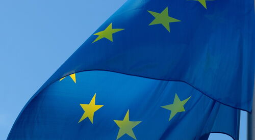 Blaue Flagge der Europäischen Union mit gelben Sternen, wehend vor blauem Himmel.