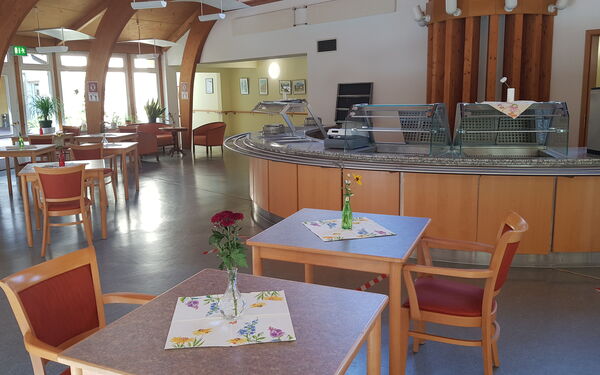 Speisesaal/Cafeteria. Halbrunder Raum, mit Theke, kleinen Tischen mit Stühlen.