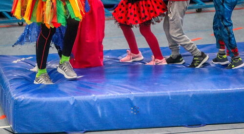 Kinderbeine in bunten Kostümen stehen auf einer blauen Turnmatte.