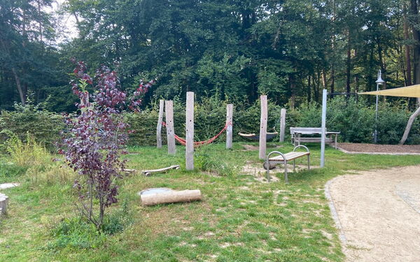 Spielplatz. Bänke stehen auf einer Wiese. Hinten im Bild ist eine Hängematte.