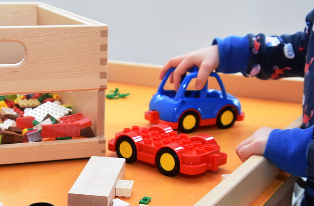 Spieletisch mit Lego und keinem Auto. Eine Kinderhand schiebt das kleine blaue Auto.