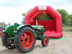 Grüner Traktor vor roter Hüpfburg.