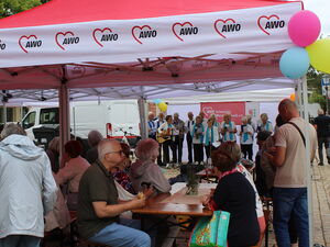 Rote AWO Pavillons mit Biertischgarnituren. Menschen die essen und trinken. Im Hintergrund der Chor.