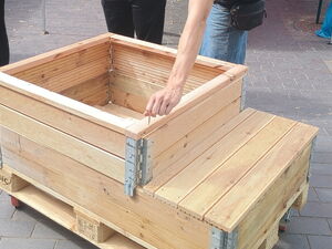 Im Innenhof ist ein AWO Pavillon davor eine Frau und ein Mann. Vor ihnen ein Hochbeet aus Holz.