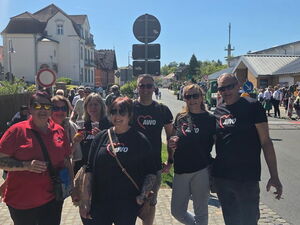 Im Ort. Sonne scheint. Menschen in AWO T-Shirt stehen auf dem Gehweg und lächeln in die Kamera. Viele Menschen sind unterwegs.