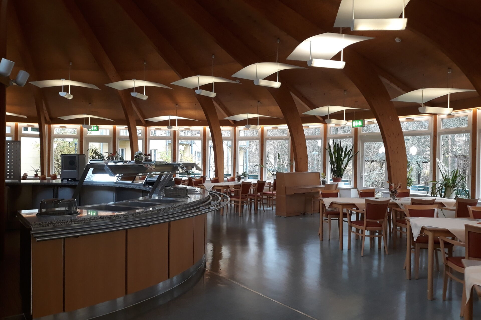 Großer Speisesaal Halb Runde Theke. Tische mit Stühlen stehen rechts an den Fenstern.