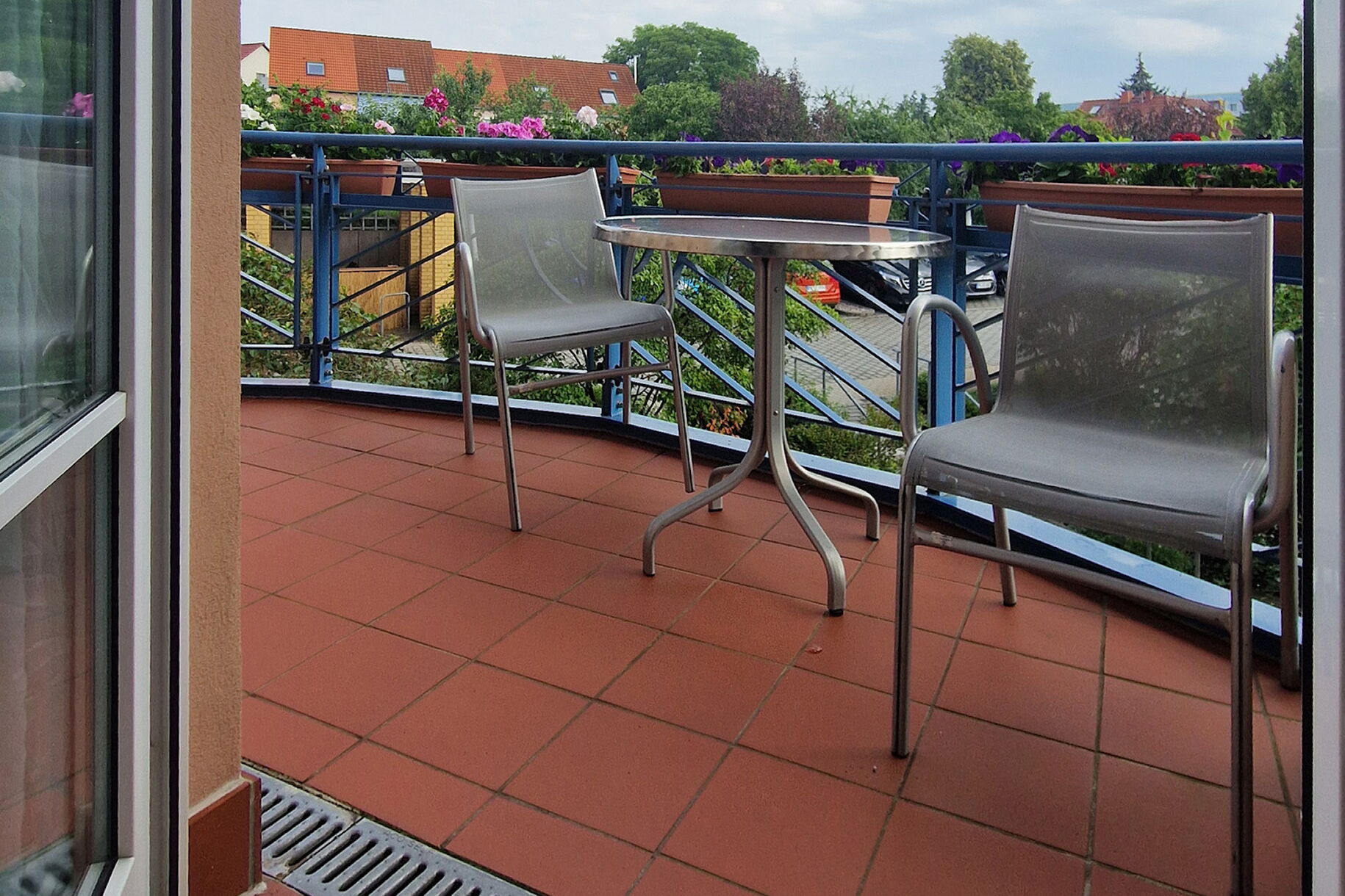 Großer halbrunder Balkon, mit Tisch und zwei Stühlen. Blick von der Balkontür nach draußen.