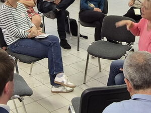 Ein großer Raum, 21 Menschen sitzen in Stuhlkreisen. In der Mitte wird diskutiert.