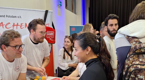 AWO Stand in einer Messehalle. 2 Männer in weißen T-Shirts mit AWWO Logo informieren eine Frau die am Stand steht.
