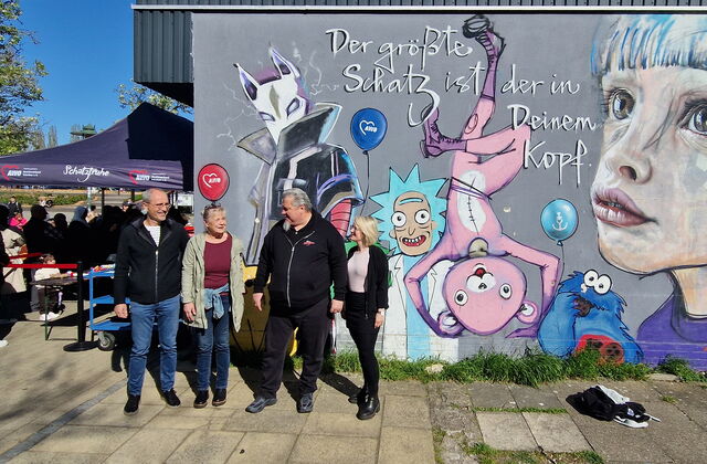 Gruppenbild. 4 Personen, 2 Männer, 2 Frauen vor eine bunten mit Figuren bemalten Graffiti Wand.