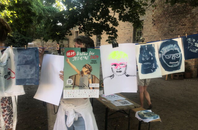 Bilder, AWO Beutel und ein Plakat von Kultur für jeden 2024 hängen an einer Wäscheleine.