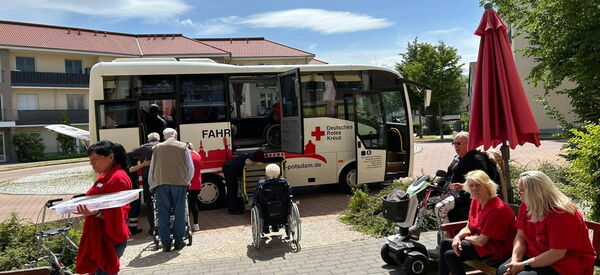 Reisebus von Deutschen Roten Kreuz steht vor Seniorenzentrum. Senioren steigen ein.
