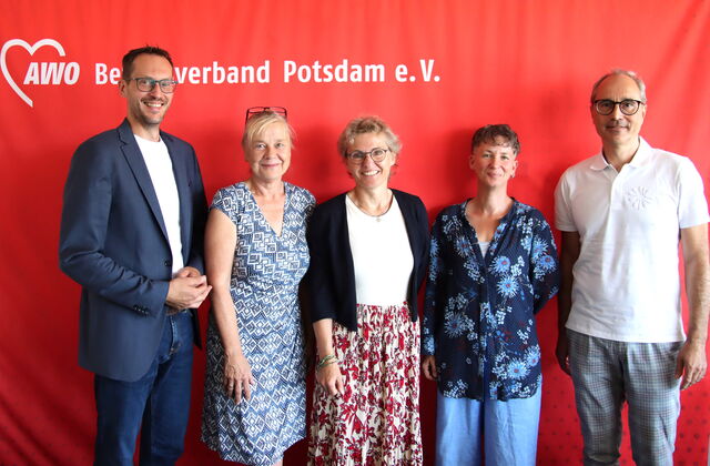 Gruppenbild, 5 Personen vor roter AWO Wand mit AWO Logo. 3 Frauen eingerahmt von zwei Männern. Alle sehen freundlich lächelnd in die Kamera.