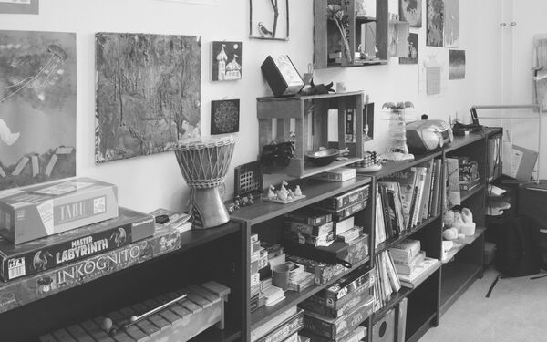 Eine Wand mit Bildern und einem langen Regal, in dem Regal sind viele Spiele, Musikinstrumente, Bücher. Das Spiel TABU, Master Labyrinth, eine Trommel