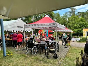 Draußen. Weißes Festzelt und rote AWO Pavillons wo Menschen sitzen. Größtenteils alte Menschen in Rollstühlen oder es stehen unweit der Tische Rollatoren.