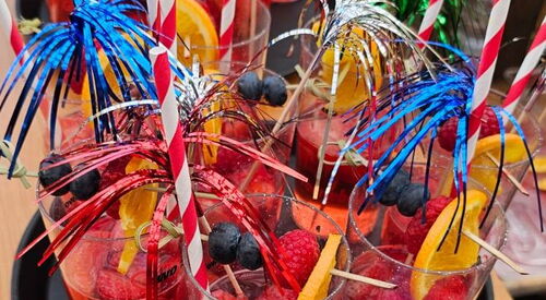 Party Gläser mit Erdbeerbowle, Strohhalmen und Deko auf einem runden Tablett.