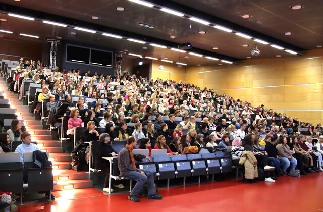 Hörsaal einer Uni. Gut besucht, fasst alle Plätze sind besetzt.