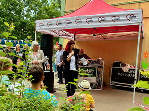 Draußen, AWO Pavillon, eine Frau mit langen roten Haaren spricht in ein Mikrofon, Erwachsene und Kinder stehen ringsherum.