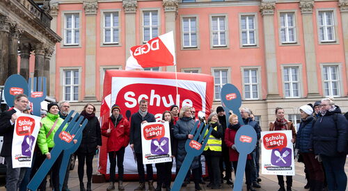 Gruppenbild. Vor dem Landtag Brandenburg. Mehrere Personen mit Schildern und großen Gabeln und Löffeln, diese sind beschriftet mit: Schule satt!