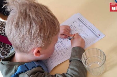 Ein kleiner blonder Junge schreibt mit einem Stift auf einem Formular