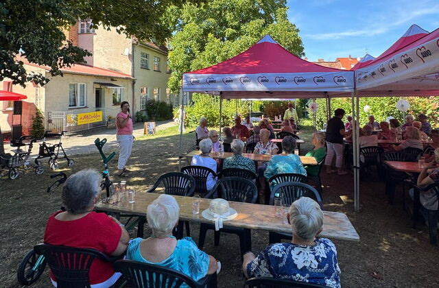 Menschen sitzen draußen im Schatten unter Bäumen und roten Pavillons.