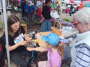 Ein Stand beim Frühlingsfest. Kleines Mädchen und ältere Frau sind bei der "Junge Plattform" Eine Frau mit schwarzem T-Shirt mit Aufdruck "AWO Junge Plattform" sitzt an einen Tisch.