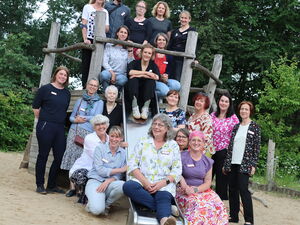 Gruppenfoto von Erwachsenen auf einem Spielplatz und Klettergerüst mit Rutsche. 20 Personen.