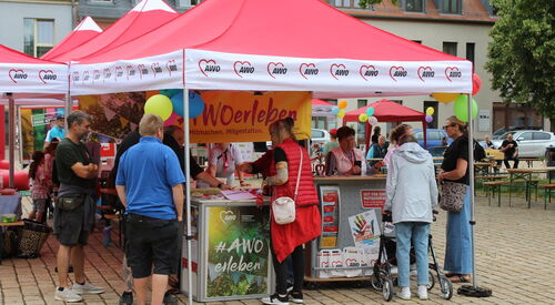 Rote AWO Pavillons: gelbes Banner: "AWO erleben"   Menschen am Stand  die sich informieren.