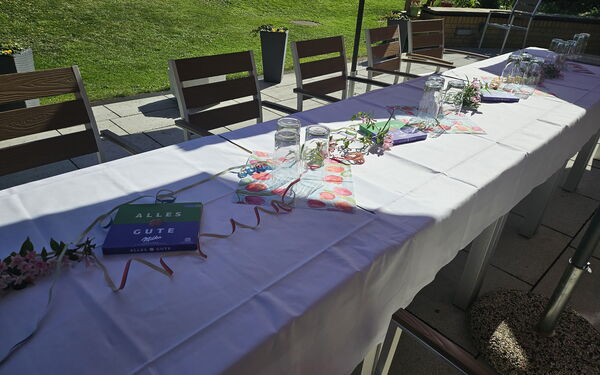 Lange Kaffeetafel auf der Terrasse, geschmückt mit Luftschlagen. Milka Schokoladenpackungen mit "Alles Gute" liegen auf dem weißen Tischtuch.