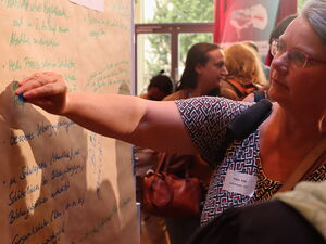Großes beschriebenes Flipchart. Teilnehmende kleben farbige Punkte zu Stichpunkten darauf.
