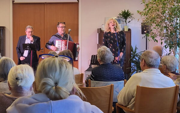 Ein Konzert. Bewohner sintzen auf Stühlen. Die Musiker und eine Sängerin stehen für dem Publikum.