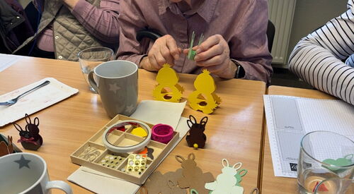 Es wird für Ostern gebastelt. Auf dem Tisch Osterhasen Vorlagen zum falten. Eine alte Frau beim basteln.