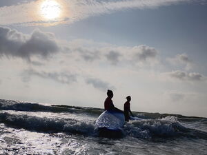 Sonne, Meer, Surfbrett und zwei Personen im Wasser.