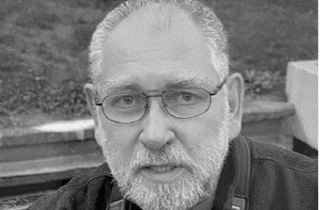 Porträt: schwarz-weiß Foto. Mann mit kurzen grauen Haare und Vollbart. Mit Brolle mit schmalem Gestell. Er trägt eine offene Jacke.