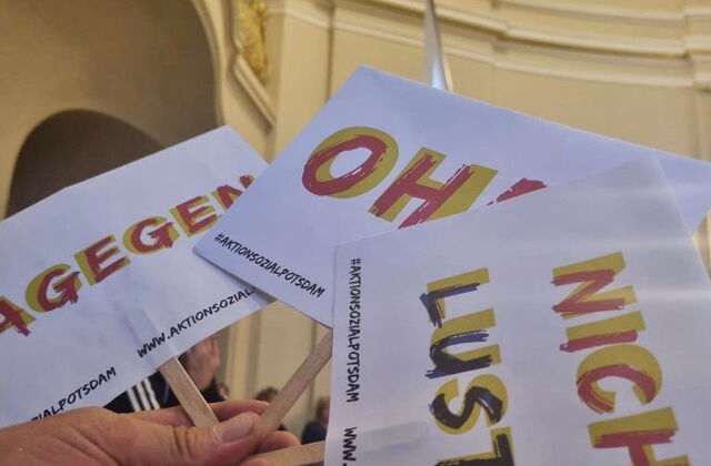 Eine Hand hält drei kleine Protestschilder in einer Hand. Auf den Schildern steht: Nicht lustig, Oha und Dagegen