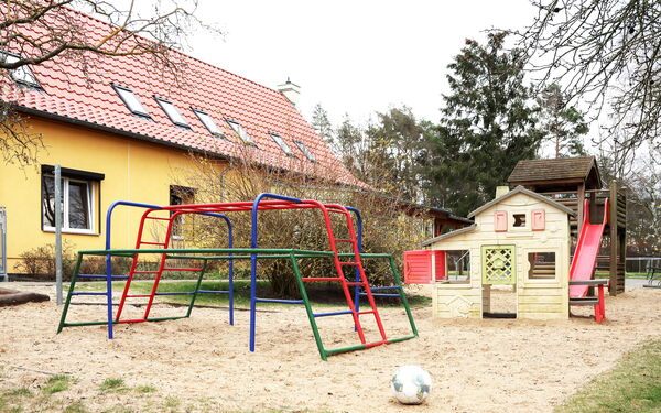 Spielplatz vor einer Kita mit verschiedenen Klettergerüsten und einem Spielhaus.