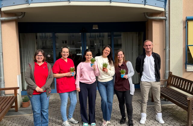 5 Frauen und ein Mann vor dem Eingang eines Seniorenzentrums. Sie jungen Frauen haben kleine Blumentöpfe in der Hand.