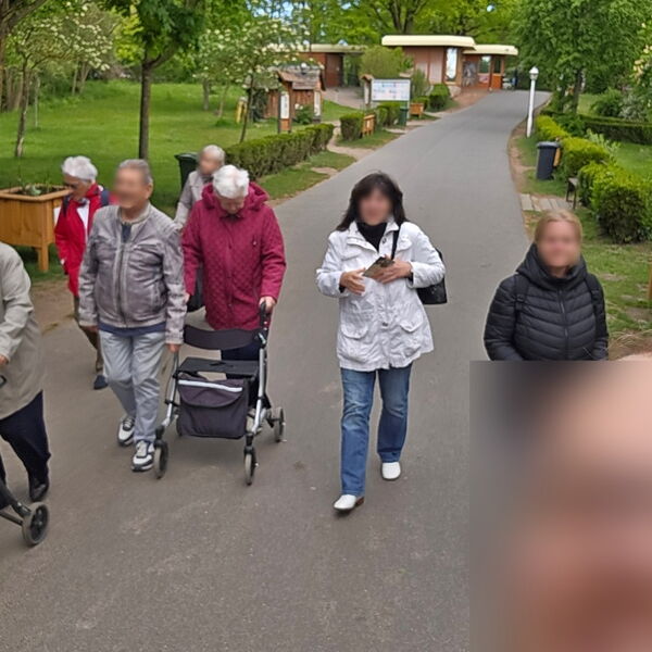 Kleine Gruppe geht einen Weg entlang. Zwei Menschen gehen am Rollator.
