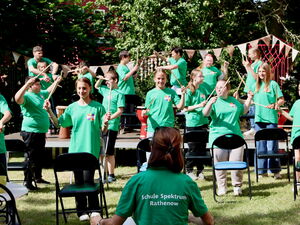 Kinder in grünen T-Shirt der Schule trommeln mit Drumsticks.