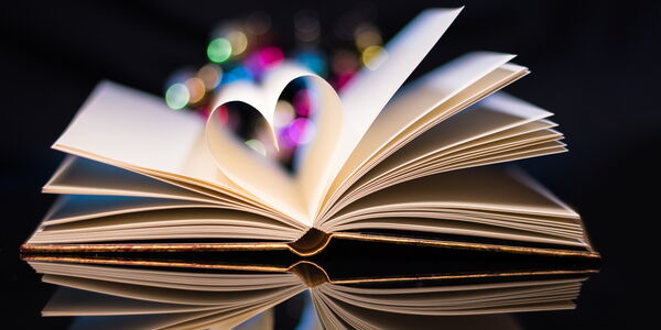 Ein aufgeschlagenes Buch, die mittleren Seiten sind zu einem Herz geformt. Der Hintergrund ist schwarz. Das Buch spielgelt sich als wenn es auf einem Spiegel liegen würde.