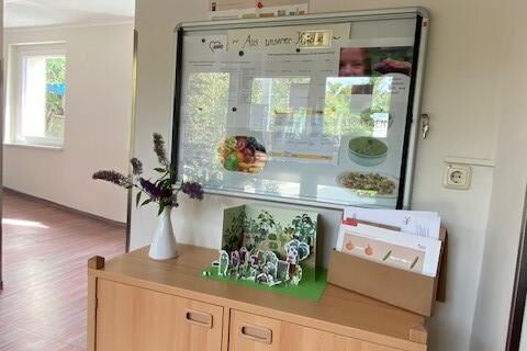 Raum mit weißen Wänden. Ein kleinen Schrank über dem eine Wandtafel hängt.