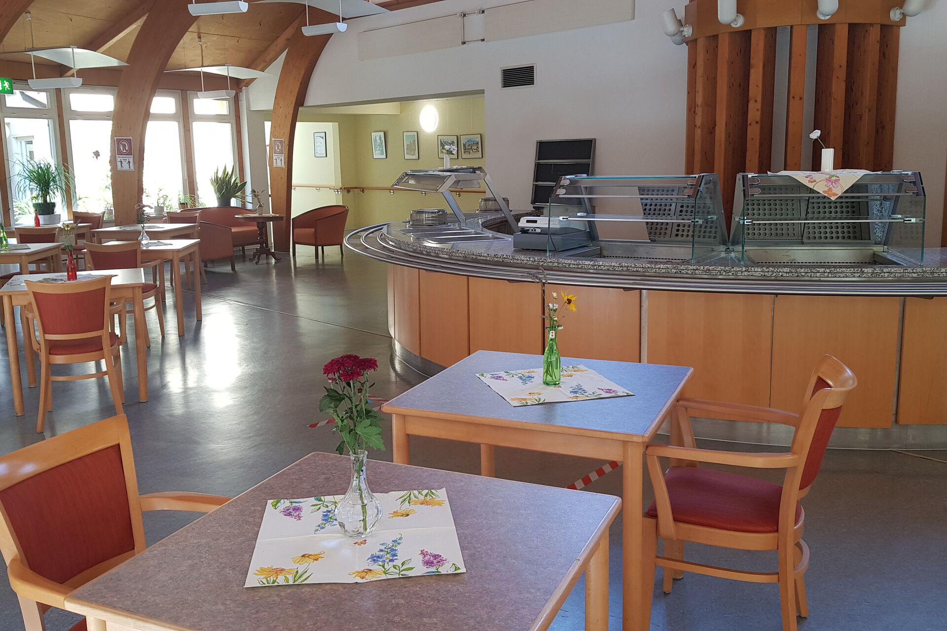 Speisesaal/Cafeteria. Halbrunder Raum, mit Theke, kleinen Tischen mit Stühlen.