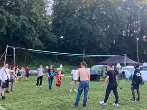 Auf dem Festivalgelände auf einer Wiese. Ein Volleyball Netz und mehrere Menschen auch ein Junge im roten T-Shirt stehen auf dem Spielfeld.