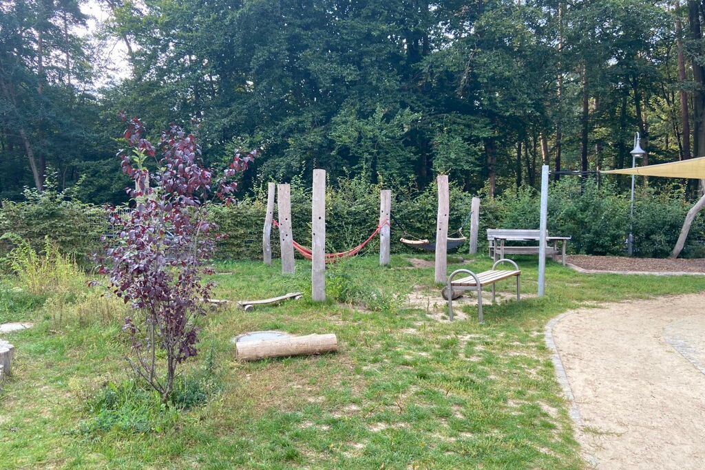 Spielplatz. Bänke stehen auf einer Wiese. Hinten im Bild ist eine Hängematte.